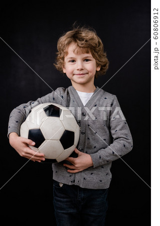 Happy little boy in casualwear holding soccer ball by chest in isolation 60806912