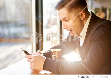 Surprised man with phone in his hand sitting near window in cafe 60806999