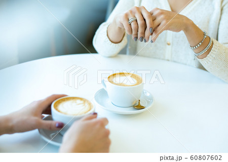 Hands of two young friendly women in casualwear having coffee at break in cafe 60807602