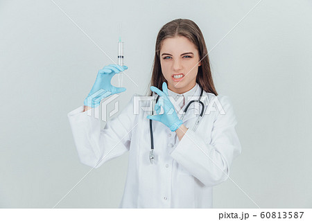 Strange female doctor holding syringes, setting teeth, looking crazily. Blurred needles on the forefront. 60813587