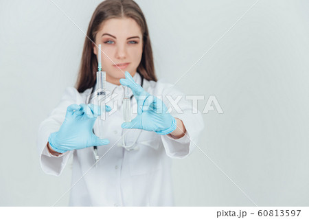 Smilng young female doctor showing to the camera two syringes, narroving her eyes. 60813597