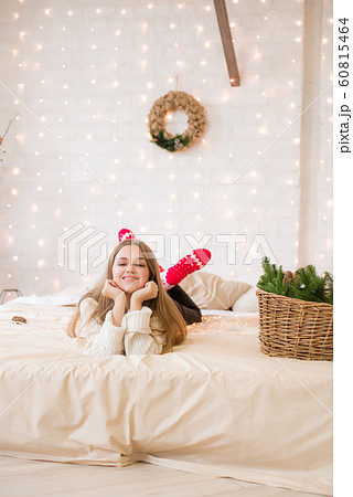 Cute teenage girl has fun at home in a light loft on the bed, decorated for Christmas with garlands and needles. Christmas mood Cute teenage girl has fun at home in a light loft on the bed, decorated for Christmas with garlands and needles. Christmas mood 60815464