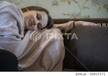 A picture of nice and thoughtful girl sits at sofa and reads a book. She has brown blanket on her shoulders. Woman got cold. She suts at window 60815571