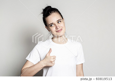 Young woman shows thumb up, smiles sweetly and good-naturedly looks at someone. Positive emotions Young woman shows thumb up, smiles sweetly and good-naturedly looks at someone. Positive emotions 60819513