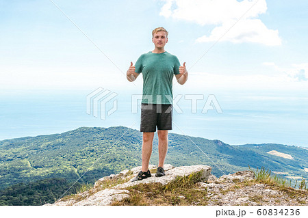 Young man standing on top of cliff in mountains Young man standing on top of cliff in mountains 60834236
