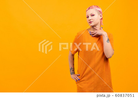 Unusual pretty woman with short pink hair and tattoo smiles isolated on orange background 60837051