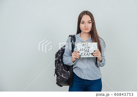 Pretty young asian girl standing, holding a sheet of paper with the prase ready for exam written on it. Backpack slung over her shoulder. 60843753