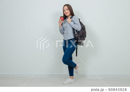 Young beautiful asian student girl standing with a backpack holding a cup of coffee. 60843928