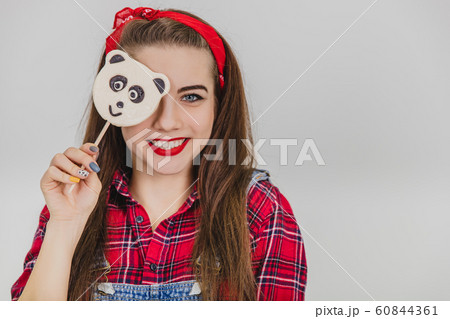 Joyful foolish girl hiding her eye behind the panda-lolly-pop, posing, smiling. Joyful foolish girl hiding her eye behind the panda-lolly-pop, posing, smiling. 60844361
