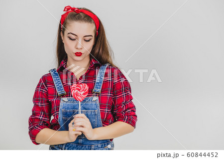 Stylish lovely enticing girl holding the red heart-shape lolly-pop on the stick, making duck face. Stylish lovely enticing girl holding the red heart-shape lolly-pop on the stick, making duck face. 60844452