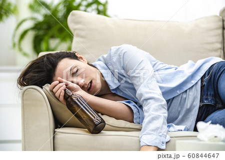 Unconscious drunk woman with empty bottle in her hand is lying on the sofa. Close up. Unconscious drunk woman with empty bottle in her hand is lying on the sofa. Close up. 60844647
