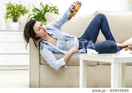 Drunk young woman is lying on the sofa and looking at empty bottle. She wants more. 60844690