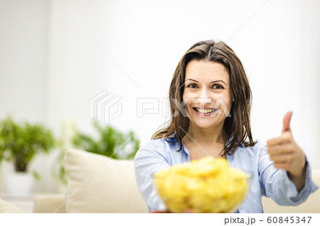 Happy adorable brunette women shows a large deep plate with potato chips snack and her thumb up. Happy adorable brunette women shows a large deep plate with potato chips snack and her thumb up. 60845347