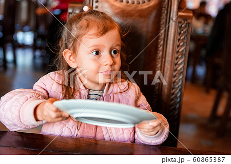 Cute preschooler girl asks for food with empty plate in hands Cute preschooler girl asks for food with empty plate in hands 60865387