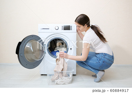 woman loads dirty clothes into washer near beige wall woman loads dirty clothes into washer near beige wall 60884917