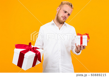 Young beautiful man holds two white boxes with gifts and chooses isolated on yellow background Young beautiful man holds two white boxes with gifts and chooses isolated on yellow background 60889215