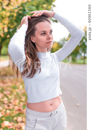Beautiful girl in autumn in park. Resting weekend in park. Emotions of comfort are pleasure and enjoyment. Autumn day portrait, warm casual wear white blouse, background trees leaves. 60901560