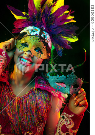 Beautiful young woman in carnival mask and masquerade costume in colorful lights Beautiful young woman in carnival mask and masquerade costume in colorful lights 60903183