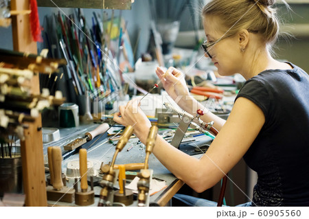 Woman artist making glass jewelry in her workshop Woman artist making glass jewelry in her workshop 60905560