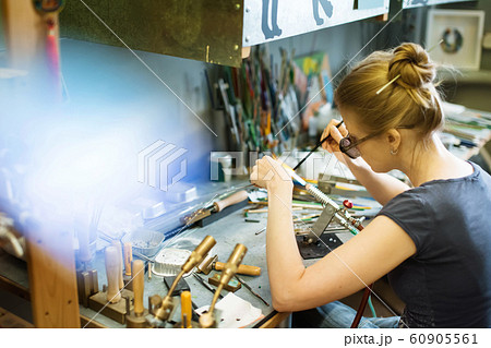 Woman artist making glass jewelry in her workshop Woman artist making glass jewelry in her workshop 60905561