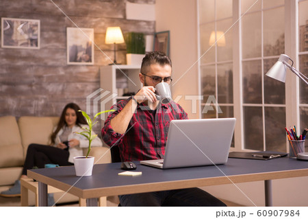 Handsome young man enjoying a cup of coffee while working on laptop 60907984