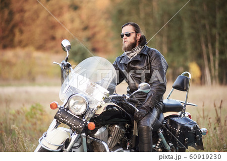Bearded biker in black leather jacket on modern motorcycle on country roadside. Bearded biker in black leather jacket on modern motorcycle on country roadside. 60919230