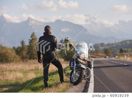 Tall athletic biker in black leather clothing standing at modern powerful high-speed motorcycle. Tall athletic biker in black leather clothing standing at modern powerful high-speed motorcycle. 60919239