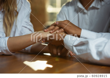 Close up of african-american and caucasian human's hands holding on wooden table Close up of african-american and caucasian human's hands holding on wooden table 60928915