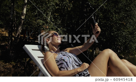Woman shooting on handheld film gimbal stabilization for smartphone. Girl lie sunbed on pier make selfie. Blogger broadcast video vlogging. 60945418
