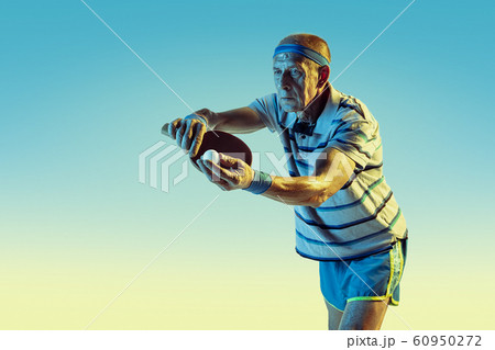 Senior man playing table tennis in sportwear on gradient background and neon light Senior man playing table tennis in sportwear on gradient background and neon light 60950272
