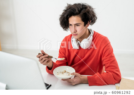 Young male freelancer having muesli with milk and watching online video 60961292