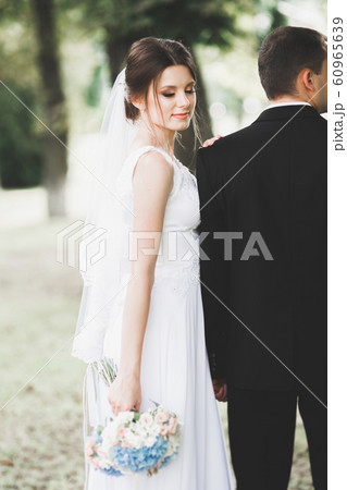 Stylish couple of happy newlyweds walking in the park on their wedding day with bouquet 60965639