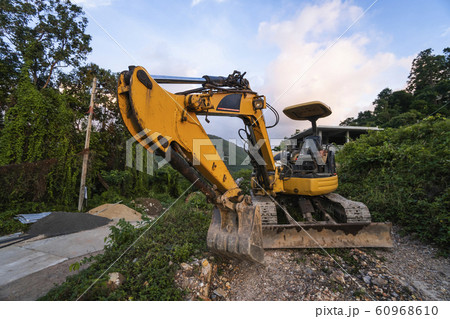 The modern excavator on the construction site with sunset sky. Large tracked excavator standing on a hill with a green grass. Machinery for a construction of a new building in the countryside. 60968610