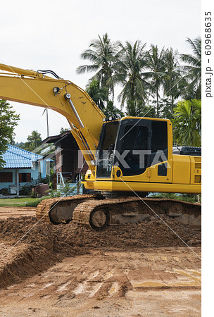 Yellow excavator on a construction site against blue sky. Heavy industry. Close up details of industrial excavator. Large tracked excavator standing on a orange ground with a palms on background. 60968635