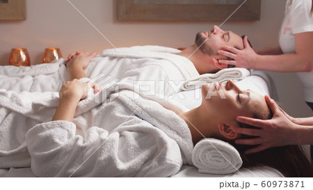 Beautiful couple lying down on massage beds enjoying a head massage in luxury spa. 60973871