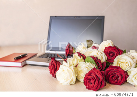 Flowers gift from fresh white and red roses at workplace on slightly pink background. On wooden table near laptop keyboard is large number of roses. Valentine concept. 60974371