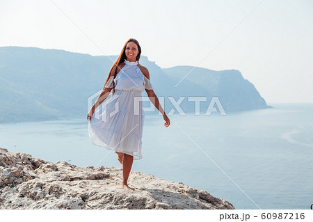 A beautiful woman with long hair in a dress looks out over the sea from a cliff 60987216