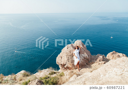 A beautiful woman with long hair in a dress looks out over the sea from a cliff 60987221