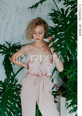 Portrait of a beautiful fashionable woman in a pink jumpsuit with green plants 60990171