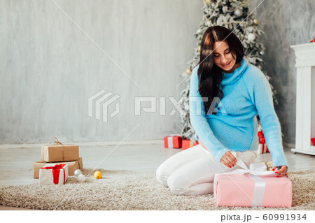 a pregnant woman sitting by the Christmas tree opens Christmas presents a pregnant woman sitting by the Christmas tree opens Christmas presents 60991934