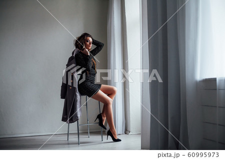 girl with gray coat sits on a Chair looking out of the window 60995973