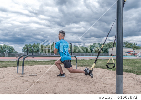 Young sportsman, male athlete, makes lunges with straps, loops for training legs, summer day city, fitness workout, active lifestyle modern youth, sportswear. Motivation life. Free space copy text. 61005972