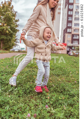 Woman mom holds the child hands, little boy son, autumn in city, warm casual clothes, grass and lawns building background. Happy smiling have a rest weekend. Woman mom holds the child hands, little boy son, autumn in city, warm casual clothes, grass and lawns building background. Happy smiling have a rest weekend. 61025882
