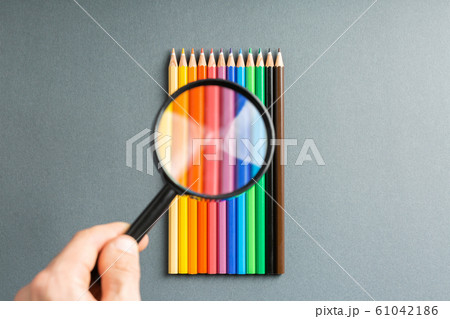 magnifier in hand over colored pencils 61042186