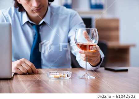 Male employee drinking alcohol and smoking cigarettes at workpla 61042803