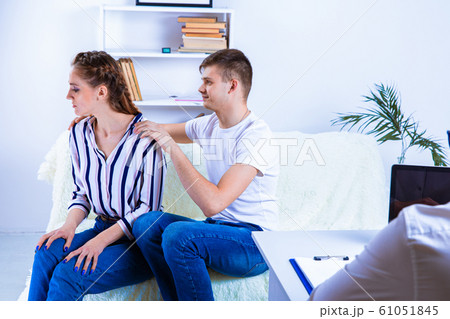 At the psychologist. Beautiful young couple is sitting on couch and hugging while doctor is making At the psychologist. Beautiful young couple is sitting on couch and hugging while doctor is making 61051845