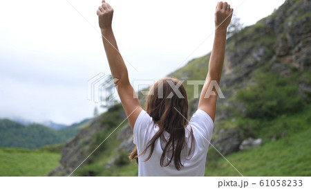 Successful young woman standing on the top of the mountain raises her hands up. Back of view Successful young woman standing on the top of the mountain raises her hands up. Back of view 61058233