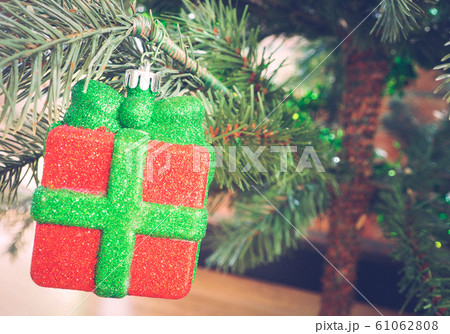 Red Christmas bauble hanging from a decorated on Christmas tree branch. Red Christmas bauble hanging from a decorated on Christmas tree branch. 61062808