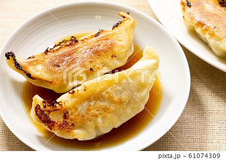 餃子のタレの入った小皿に入れられた焼き餃子。 61074309
