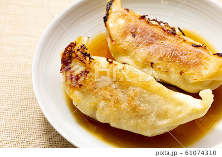 餃子のタレの入った小皿に入れられた焼き餃子。 餃子のタレの入った小皿に入れられた焼き餃子。 61074310